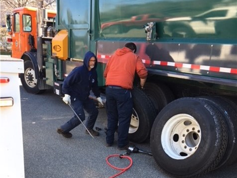 Picture shows Public Works employees performing repairs on a solid waste truck.  